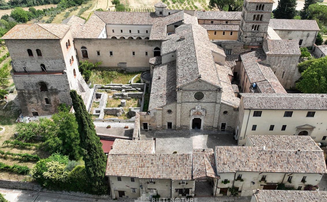 Vista aerea dell'Abbazia di Farfa, con la sua maestosa architettura e i chiostri interni, circondata dalla campagna sabina.