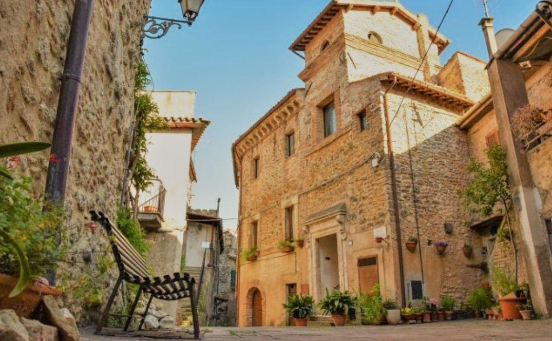 Vicolo storico di Montopoli di Sabina con edifici in pietra, una sedia in metallo e piante in vaso