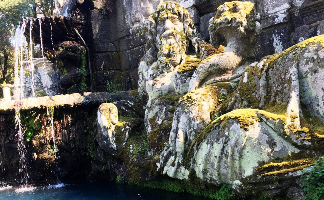 Dettaglio di una scultura muschiosa raffigurante figure mitologiche in una fontana storica, probabilmente situata nel complesso di Vescovio o una villa vicina.